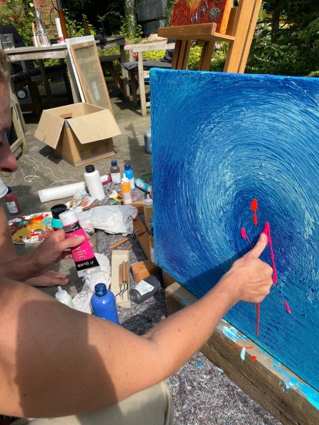 Eine Person malt mit leuchtenden Farben auf eine Leinwand im Freien.